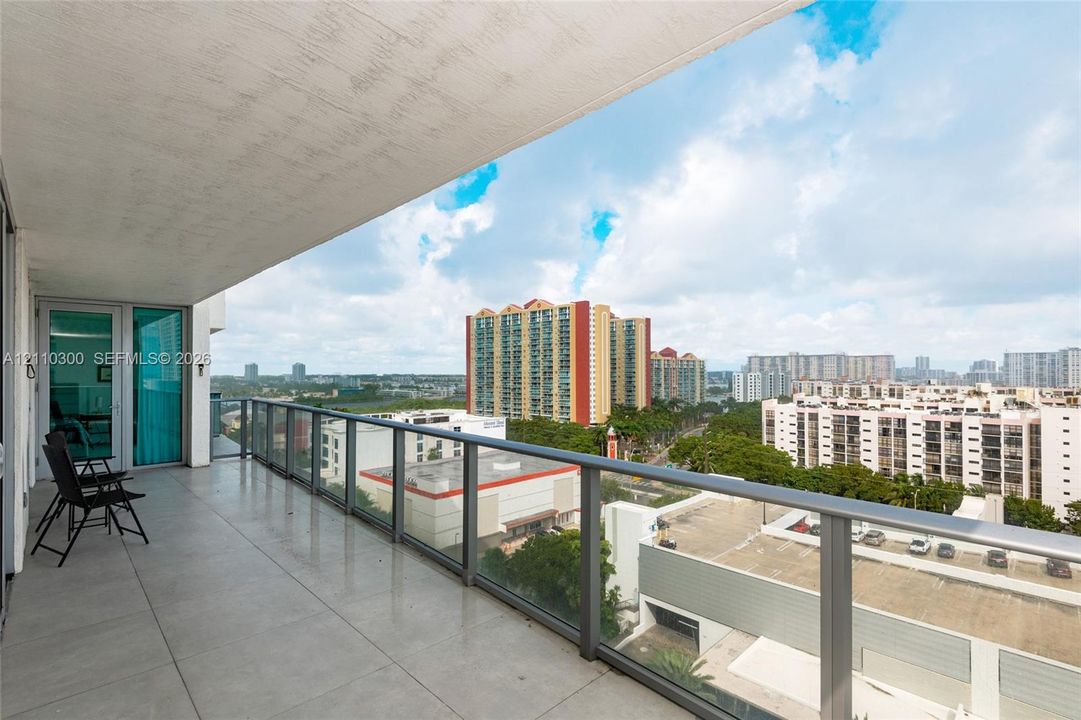 Covered balcony with large-format tile flooring, glass railing system, and floor-to-ceiling sliding glass doors