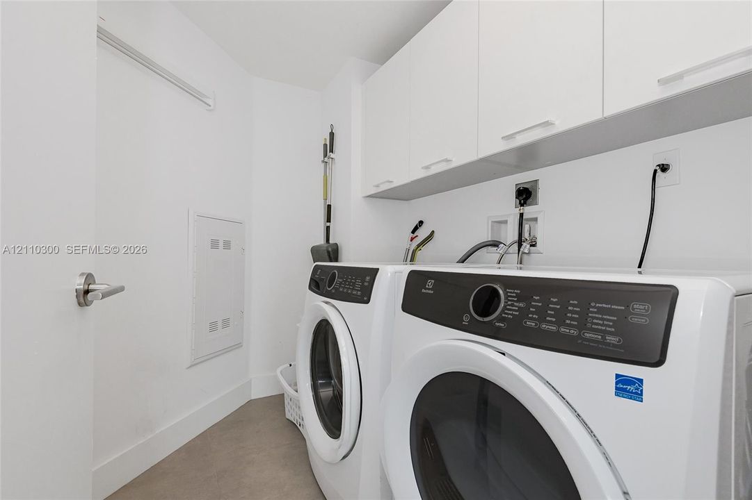 Laundry area featuring custom white upper cabinetry, stainless steel-trimmed appliances, and smooth-finish flooring