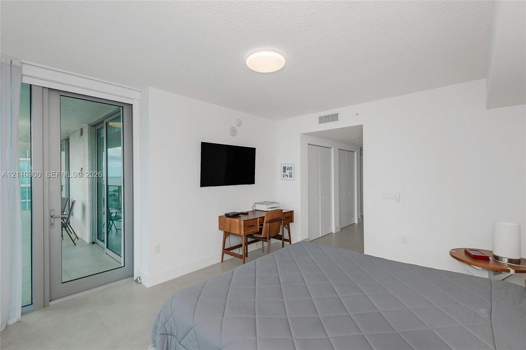 Master Bedroom. Neutral-toned tile flooring, large sliding glass door with access to a balcony, and dual bi-fold closet doors