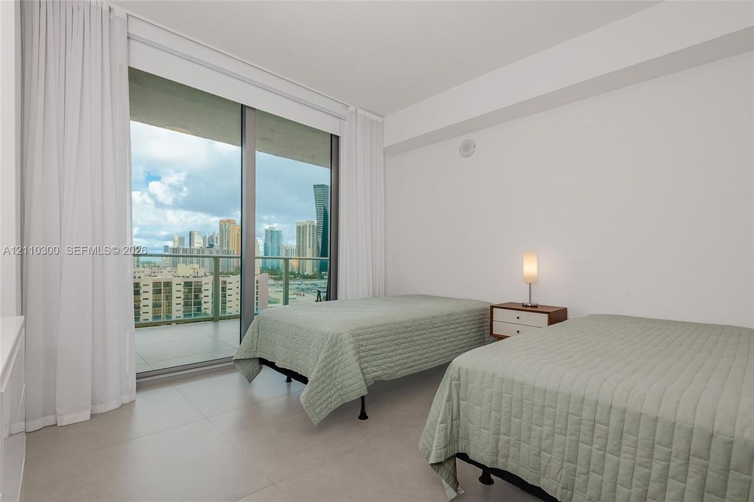 Bedroom 2. Floor-to-ceiling glass sliding doors, private balcony, neutral large-format tile flooring, and flush-mount ceiling lighting