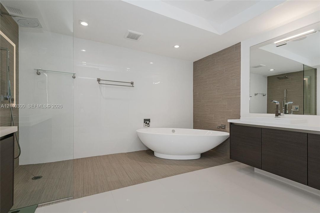 Master Bathroom  Freestanding soaking glass-enclosed walk-in shower, wall-mounted dark wood-finish cabinetry with quartz countertop, and recessed lighting