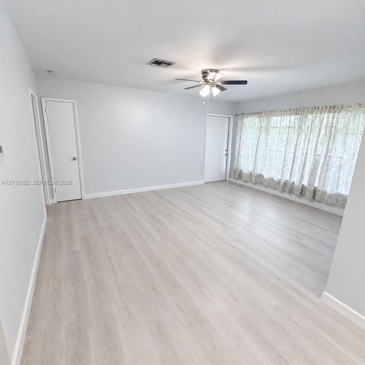 Neutral interior space featuring wood-finish flooring, a ceiling fan with integrated lighting, and expansive window coverage