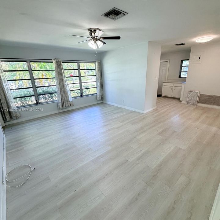 Light-filled interior featuring wood-finish flooring, a multi-pane window system, ceiling fan with integrated lighting, and cabinetry with neutral countertops