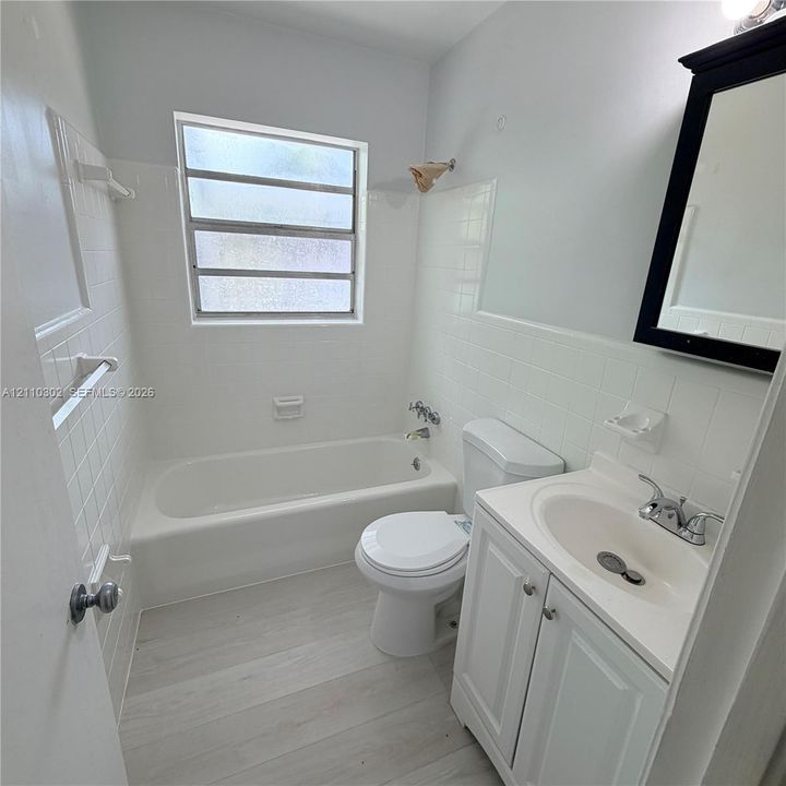 Bathroom featuring wood-finish flooring, white tile wall surround, built-in soaking tub, and vanity with an integrated basin and chrome hardware