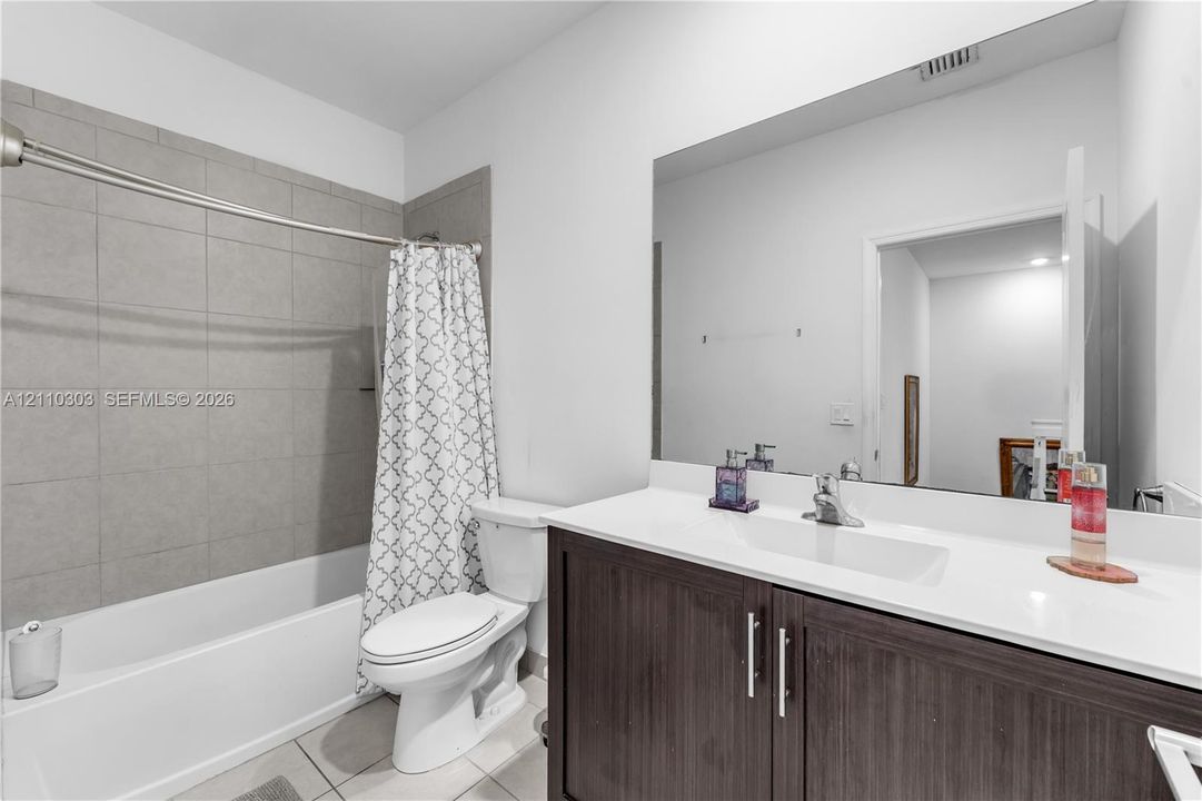 Bathroom featuring a dark wood-finish vanity with a white countertop and integrated sink, a full-width wall mirror, and a tub-shower combination with large-format grey tile surround