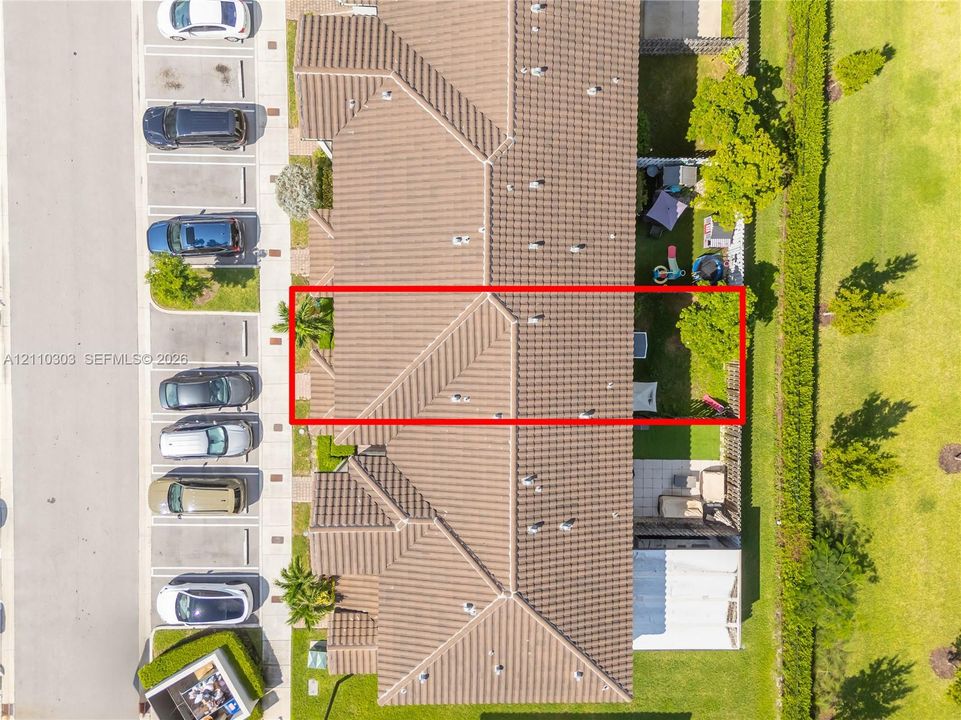 Aerial view featuring a multi-unit structure with a tiled roof, designated surface parking, and a private rear yard space