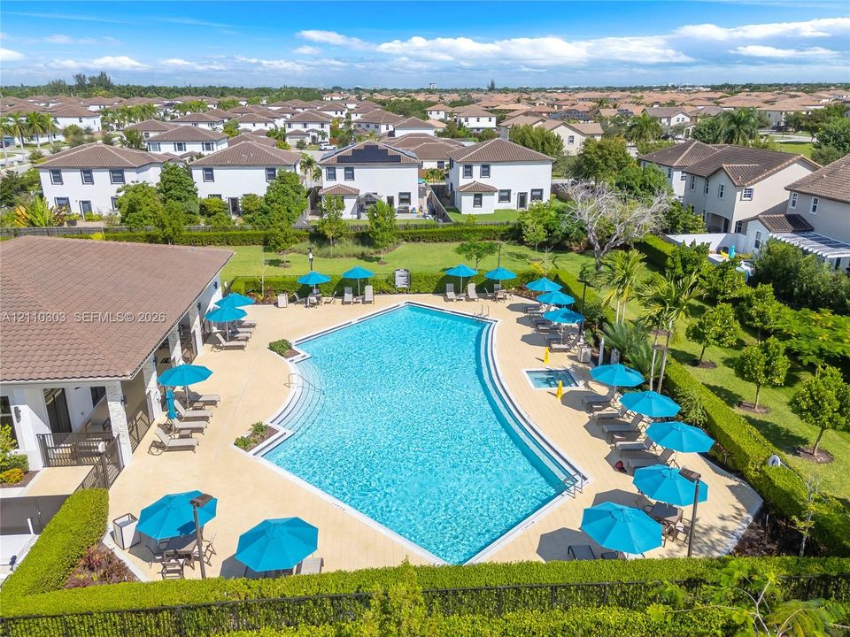Community amenity area featuring a swimming pool, integrated spa, tiled pool deck, and manicured perimeter landscaping