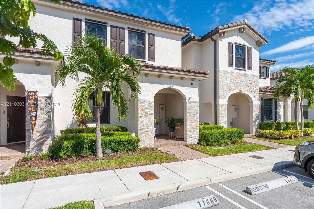 Stucco exterior featuring stacked stone accents, arched covered entryways, dark shuttered windows, tile roofing, and manicured shrubbery