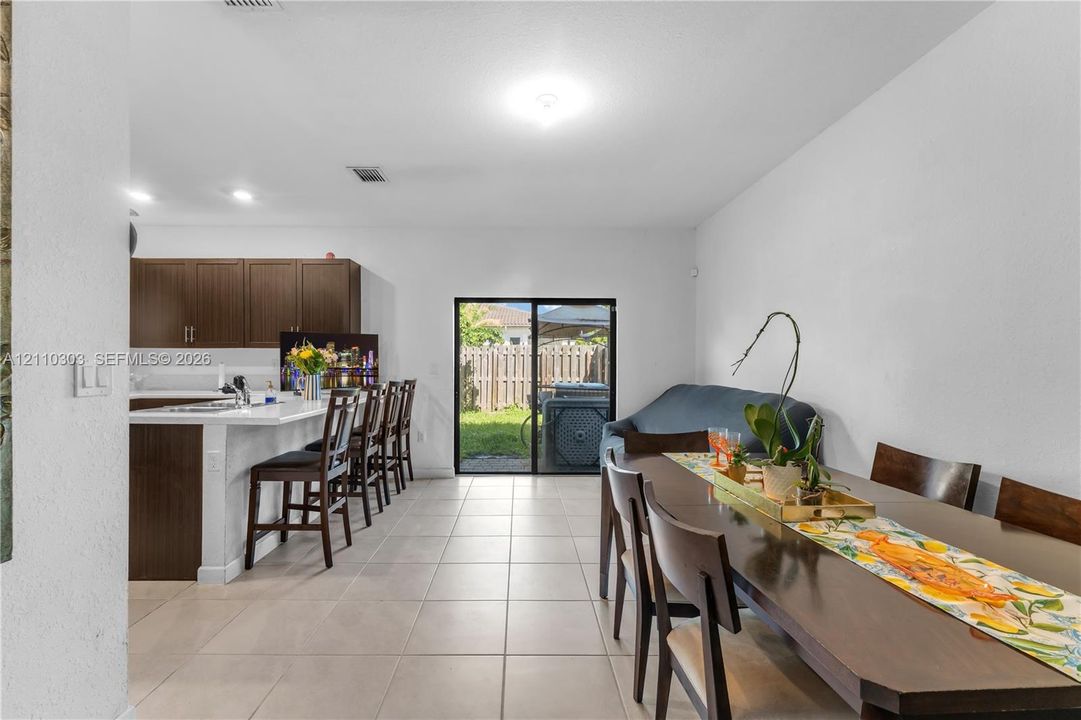 Open-concept kitchen featuring stained wood cabinetry, quartz countertops, a spacious breakfast bar, neutral tile flooring, and sliding glass doors
