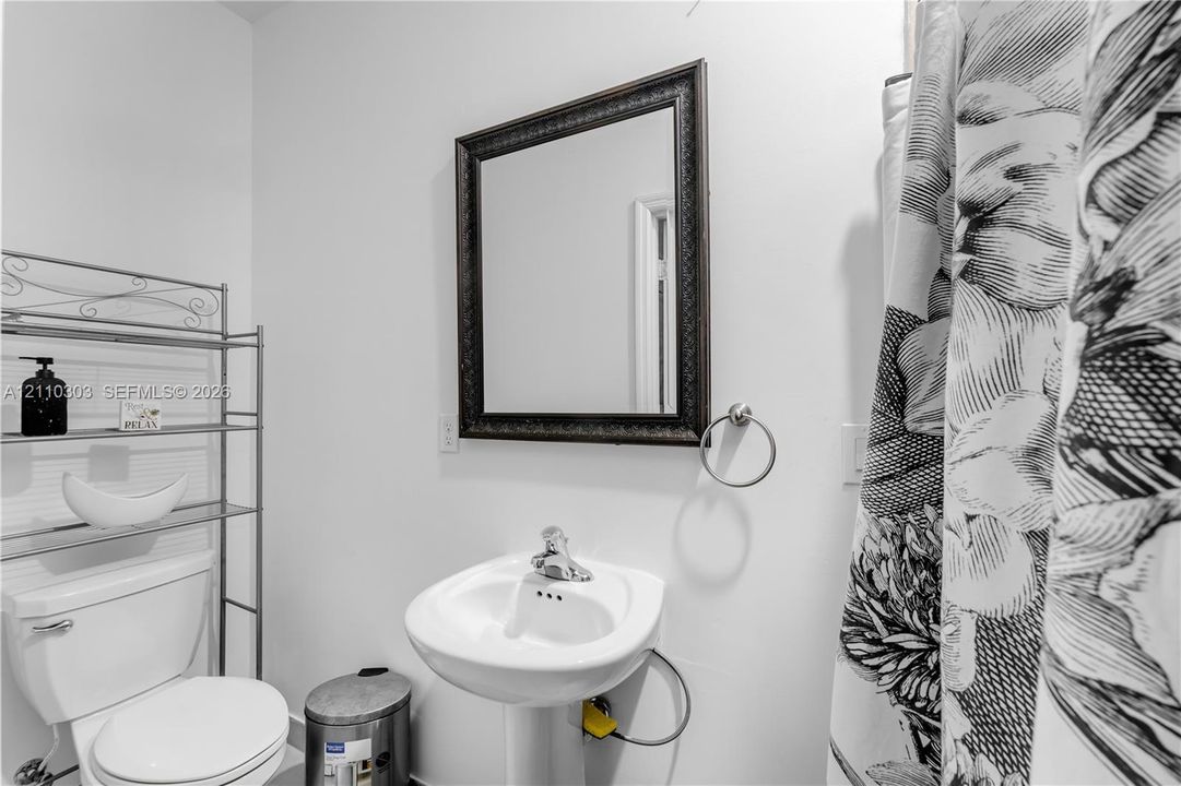Wall-mounted framed mirror, pedestal sink with chrome-finish faucet, and circular towel ring