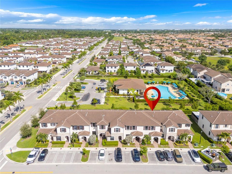Aerial perspective featuring a multi-unit residential building with a tiled roof, assigned parking spaces, and proximity to a community swimming pool