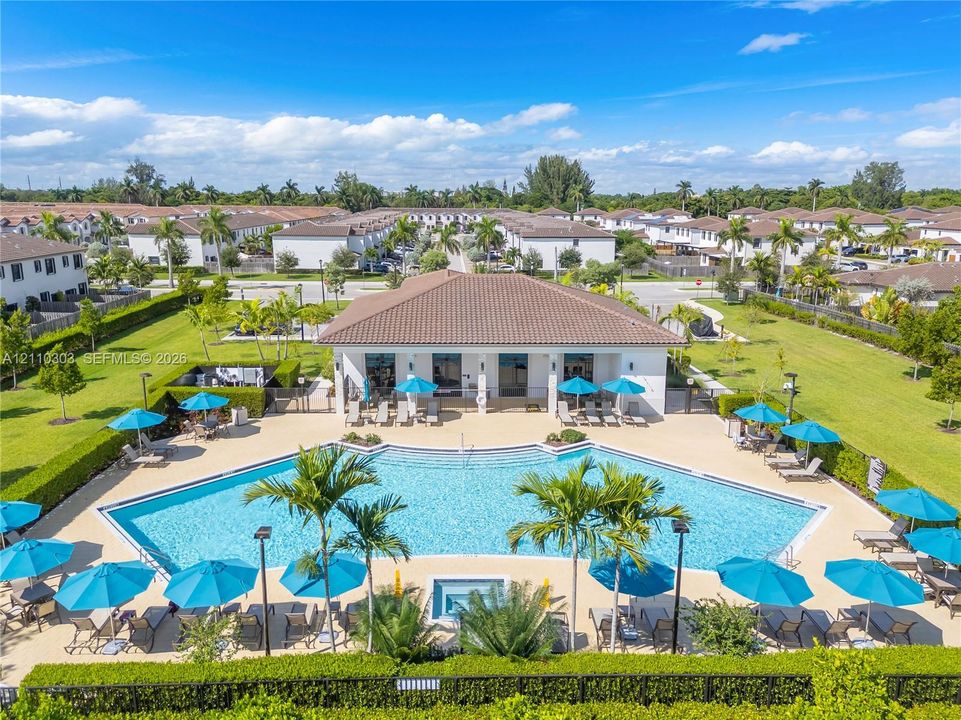 Community swimming pool featuring a sprawling sun deck, built-in hot tub, landscaped lawn, and manicured perimeter hedges