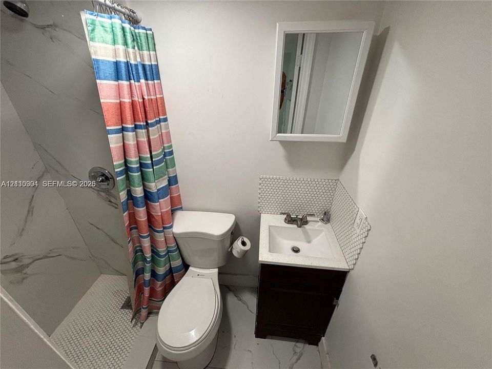 Shower with stone-finish wall tile, vanity cabinet featuring a solid surface countertop, hex-tile backsplash, and wall-mounted medicine cabinet