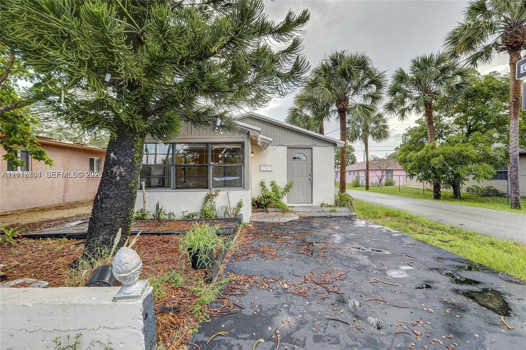 Exterior featuring a light-toned stucco façade, multi-pane windows, and a paved driveway, accented by mature palm trees and established landscaping