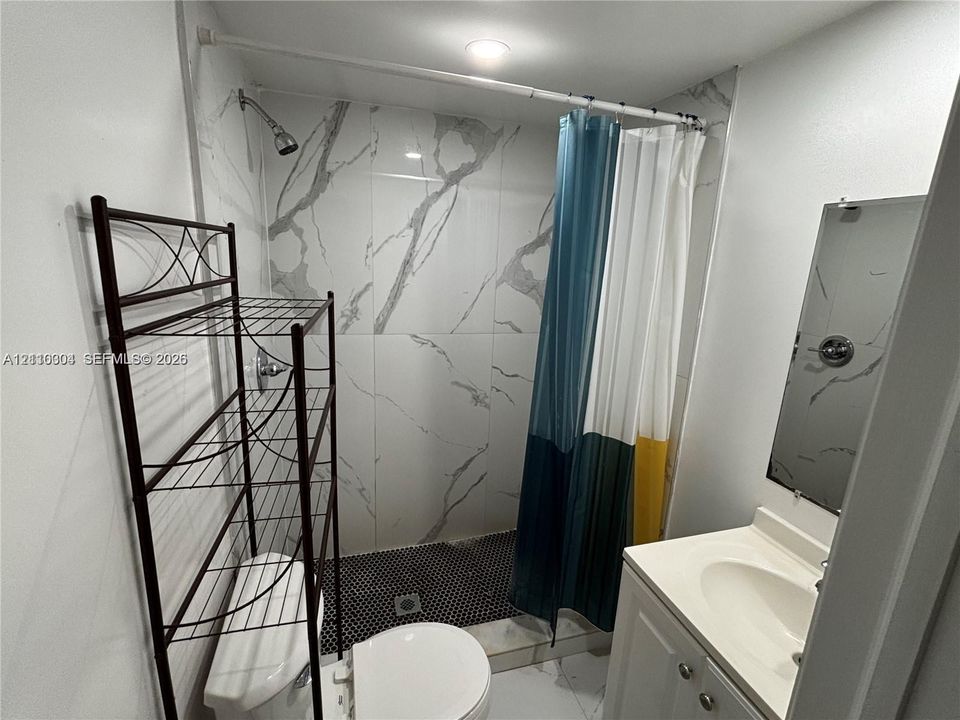 Full-height stone-finish wall tile, walk-in shower with mosaic tile flooring, vanity with integrated sink, and wall-mounted mirror