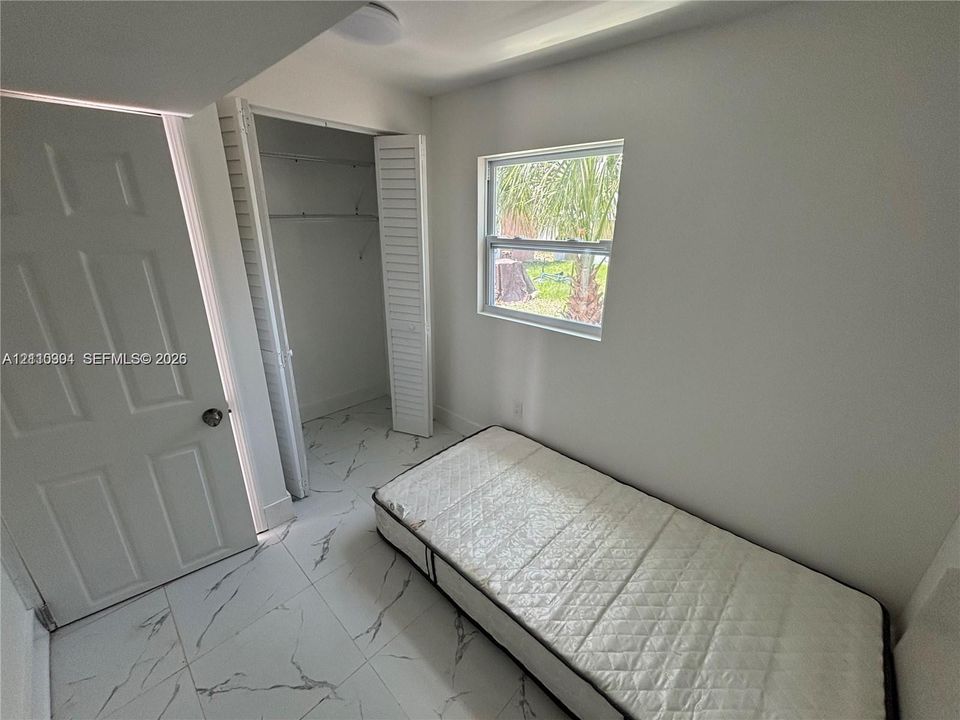 Neutral-toned room featuring large-format tile flooring with marbling detail, single-pane window, and closet with louvered double doors