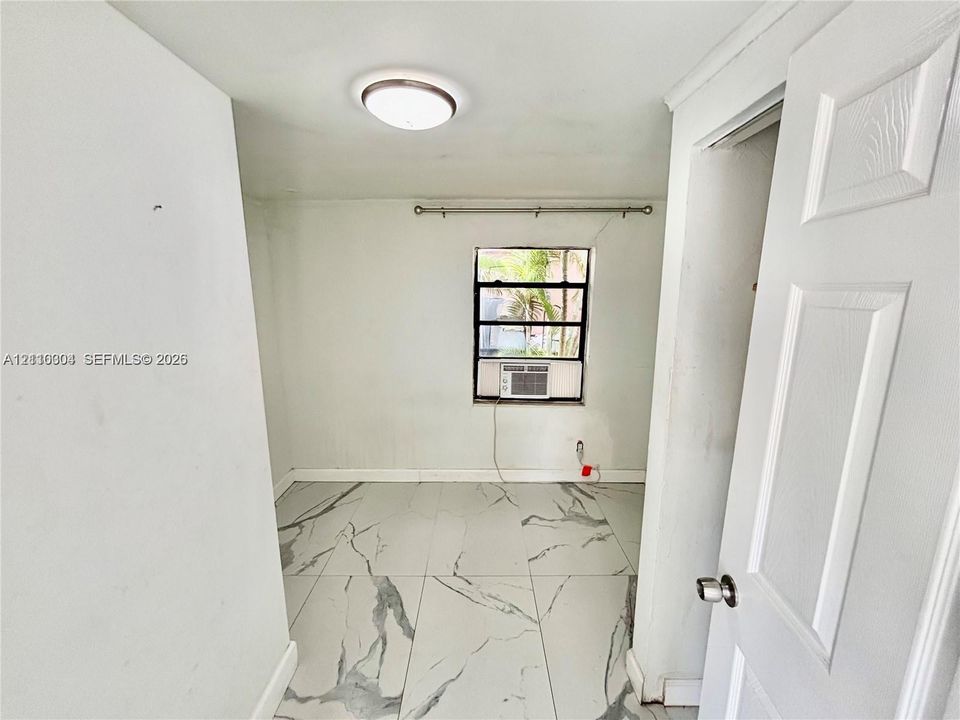 Large-format veined tile flooring, flush-mount circular lighting fixture, and a single-hung window with a mounted window air conditioning unit