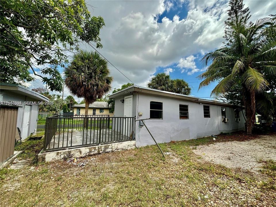 Exterior space featuring a concrete patio enclosed by metal fencing, neutral-toned stucco siding, and mature palm trees