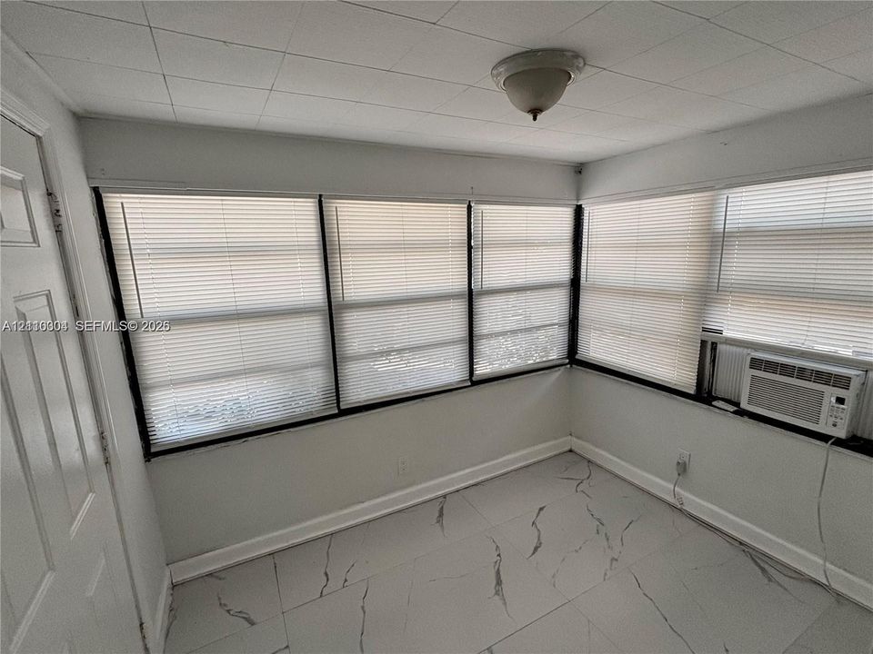 Large-format stone-pattern tile flooring, multiple windows with integrated blinds, and an installed wall-mounted air conditioning unit