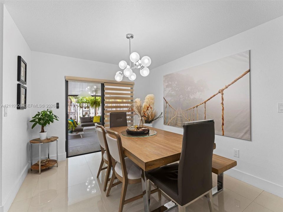 Dining area featuring polished tile flooring, contemporary multi-globe light fixture, and sliding glass door with integrated window treatments