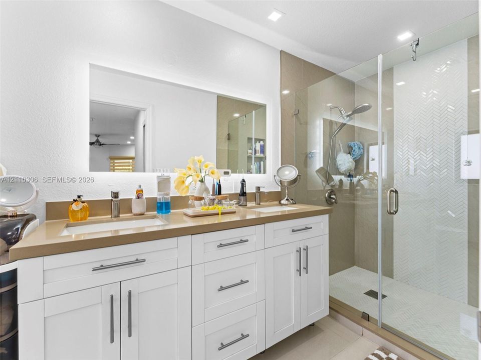 Double vanity featuring white cabinetry, quartz-style countertops, rectangular undermount sinks, and a backlit mirror