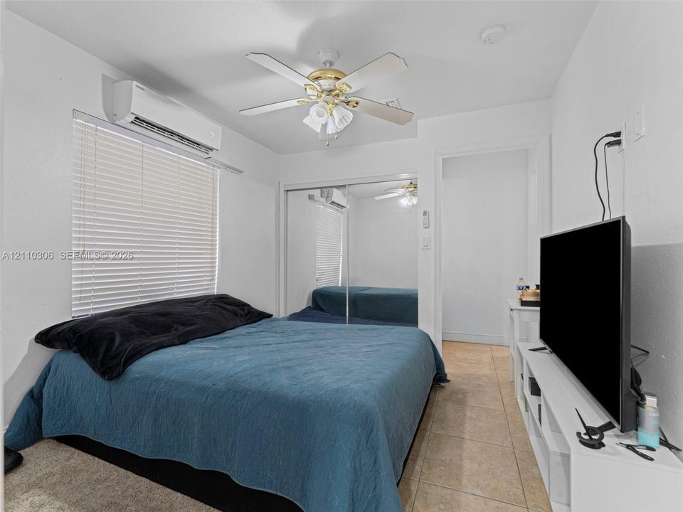 Wall-mounted climate control unit, ceiling fan with integrated lighting, mirrored sliding closet doors, and tile flooring