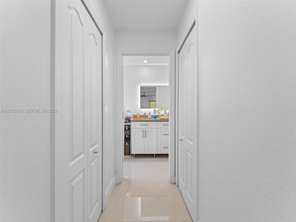 Hallway featuring dual bifold doors, polished tile flooring, and a vanity with white shaker-style cabinetry and a backlit mirror