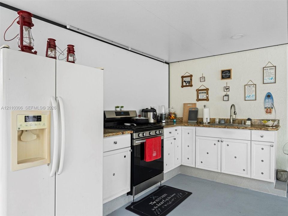 Kitchen featuring white cabinetry with circular hardware, stone-finish countertops, stainless steel gas range, and integrated white refrigerator