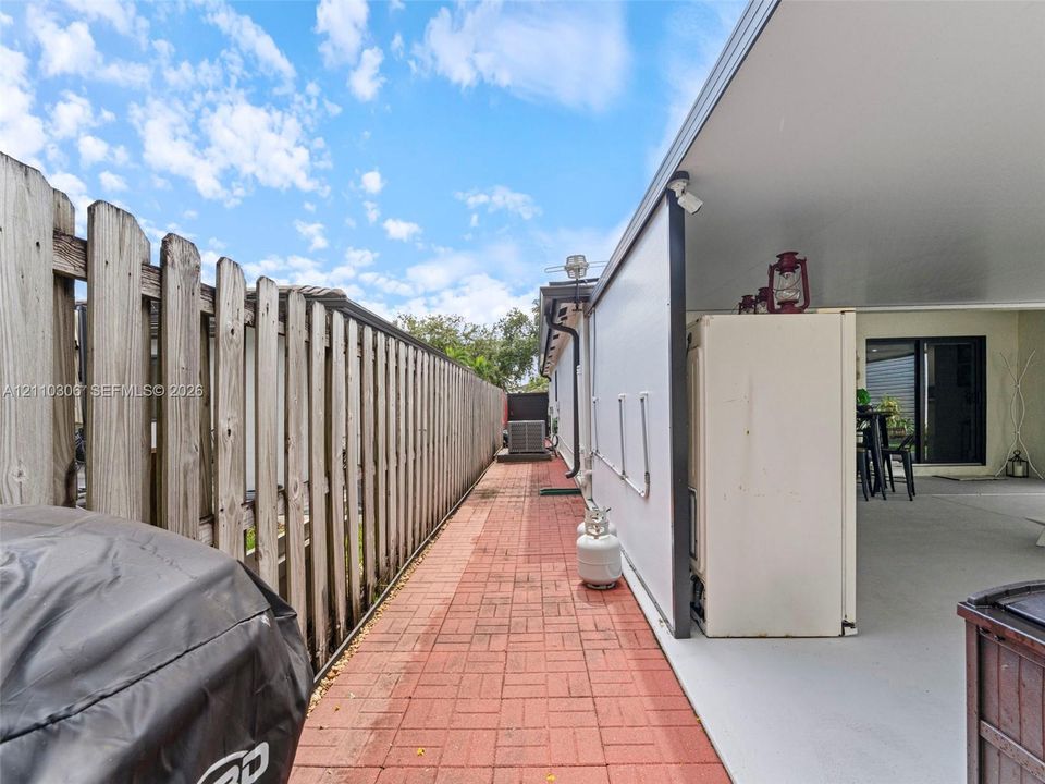 Side exterior area featuring a concrete-paved patio, red brick-style pavers, and a full-height wood privacy fence