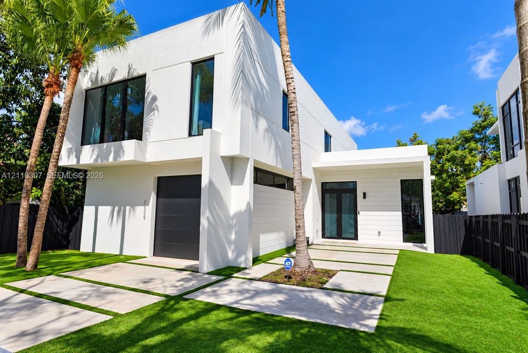 Modern exterior featuring white smooth-stucco facade, black-framed windows, integrated garage door, and a geometric concrete paver driveway with turf accents