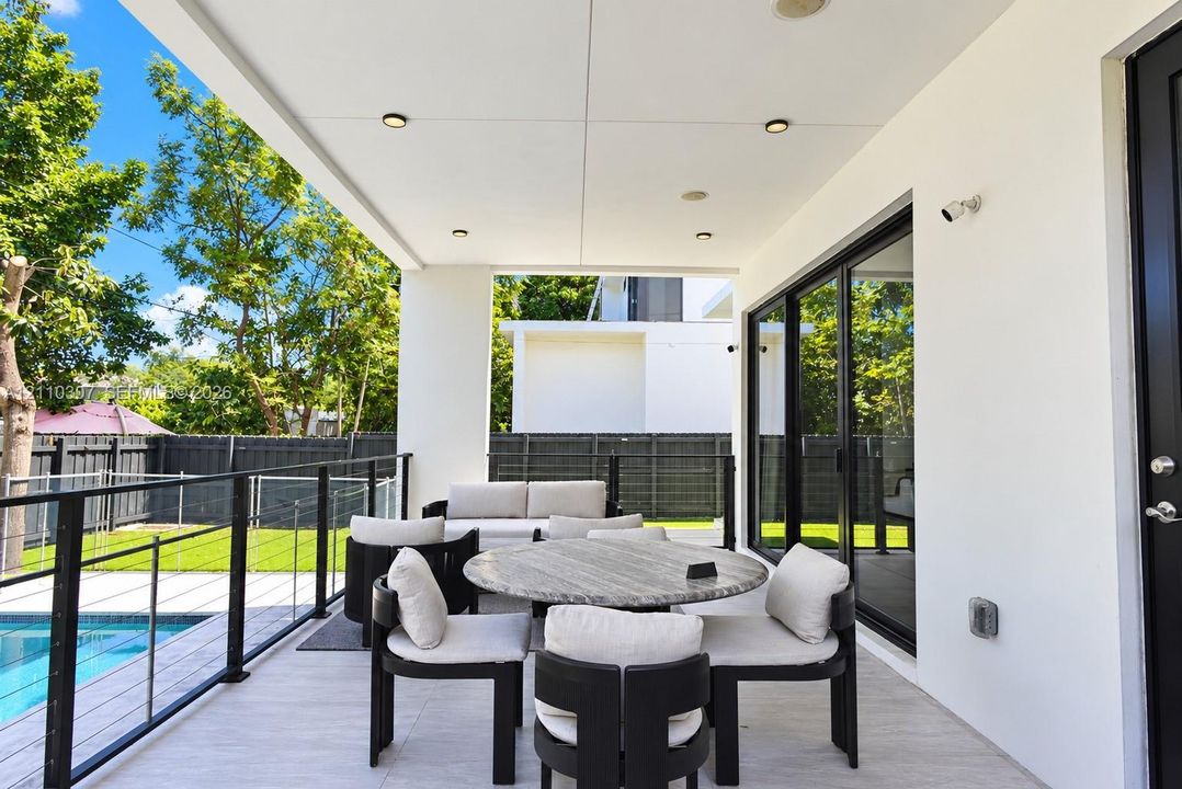 Covered patio featuring recessed lighting, tile flooring, and a glass-paneled railing overlooking the swimming pool