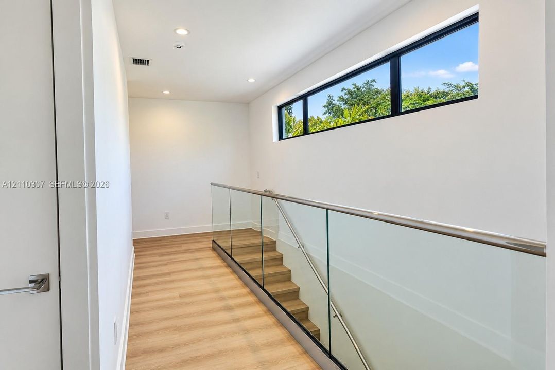 Hallway featuring wood-finish flooring, recessed lighting, a horizontal clerestory window, and a glass panel railing with a metallic handrail