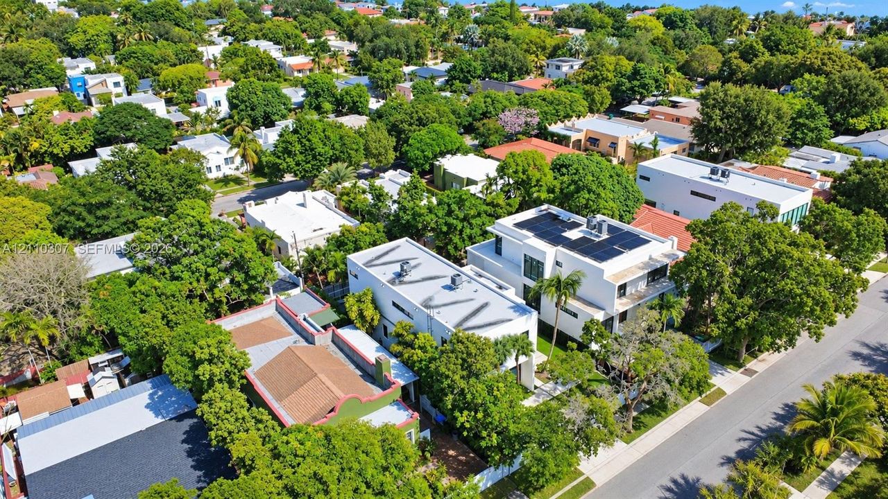 Aerial perspective of a multi-story residence featuring a flat roofline, roof-mounted solar panels, integrated HVAC units, and mature canopy trees