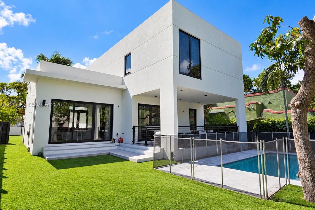 Modern architectural exterior featuring smooth stucco finish, floor-to-ceiling black-framed windows, covered patio area, private swimming pool, and manicured lawn