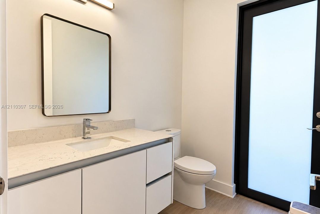 Modern vanity featuring a stone-composite countertop, rectangular undermount sink, matte black-framed mirror, and frosted glass paneled door
