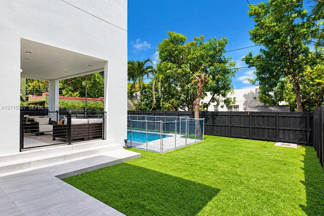 Covered patio featuring recessed lighting, a fenced swimming pool with stone surround, and a lawn enclosed by black wood fencing