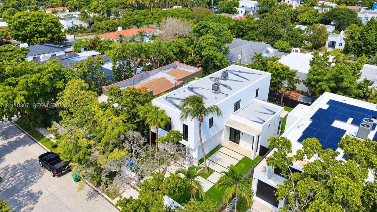 Two-story contemporary exterior featuring a flat roofline, paved driveway with grass inserts, and mature palm landscaping