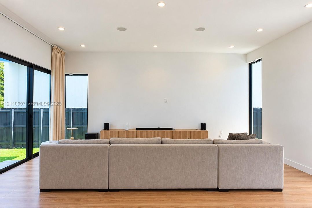 Living area featuring wood-finish flooring, recessed lighting, floor-to-ceiling glass sliding doors, and custom wood-slatted built-in cabinetry