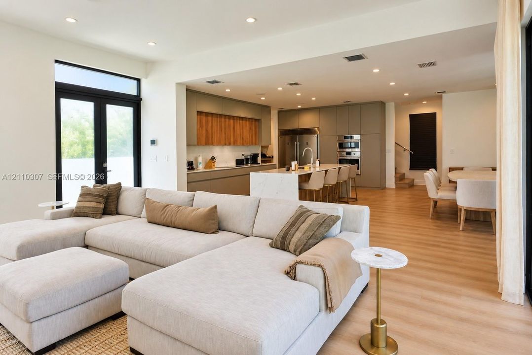 Kitchen featuring an expansive center island with waterfall edge, flat-panel cabinetry, built-in stainless steel appliances, and wood-finish flooring throughout