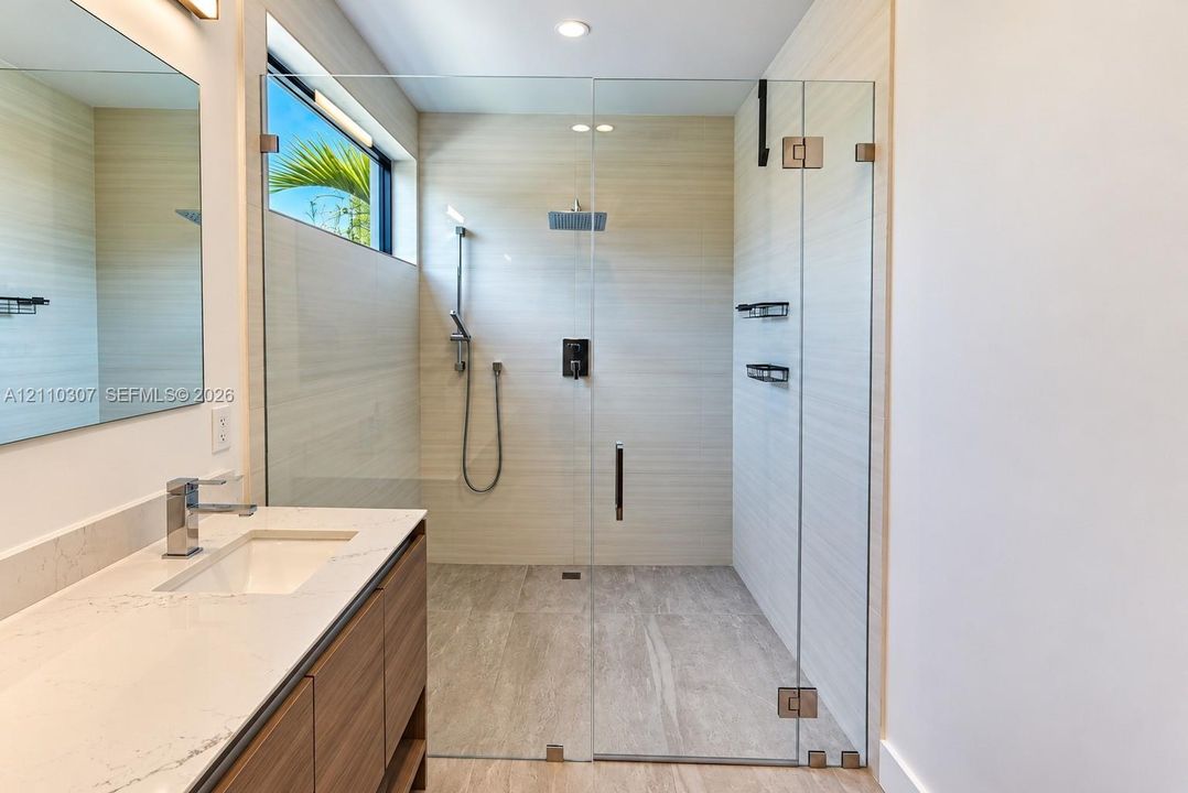 Bathroom featuring a wood-finish floating vanity with a stone countertop, an integrated rectangular sink, a glass-enclosed walk-in shower with horizontal wall tile, and a rainfall showerhead