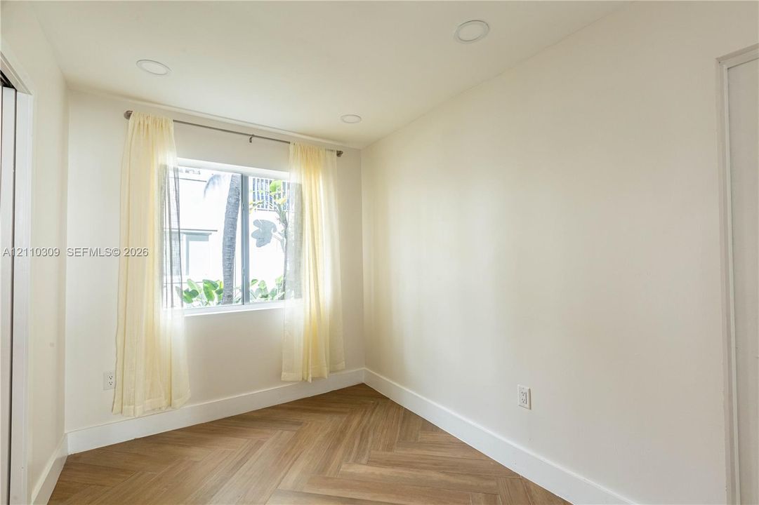 Interior space featuring herringbone-patterned wood-finish flooring, recessed ceiling lighting, and a single-pane window with metal framing