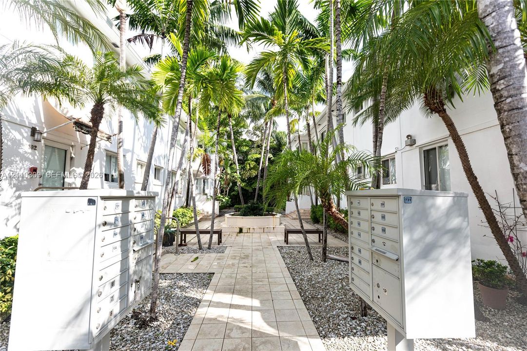 Courtyard featuring stone-tile hardscaping, mature palm trees, gravel accents, and built-in metal mail centers