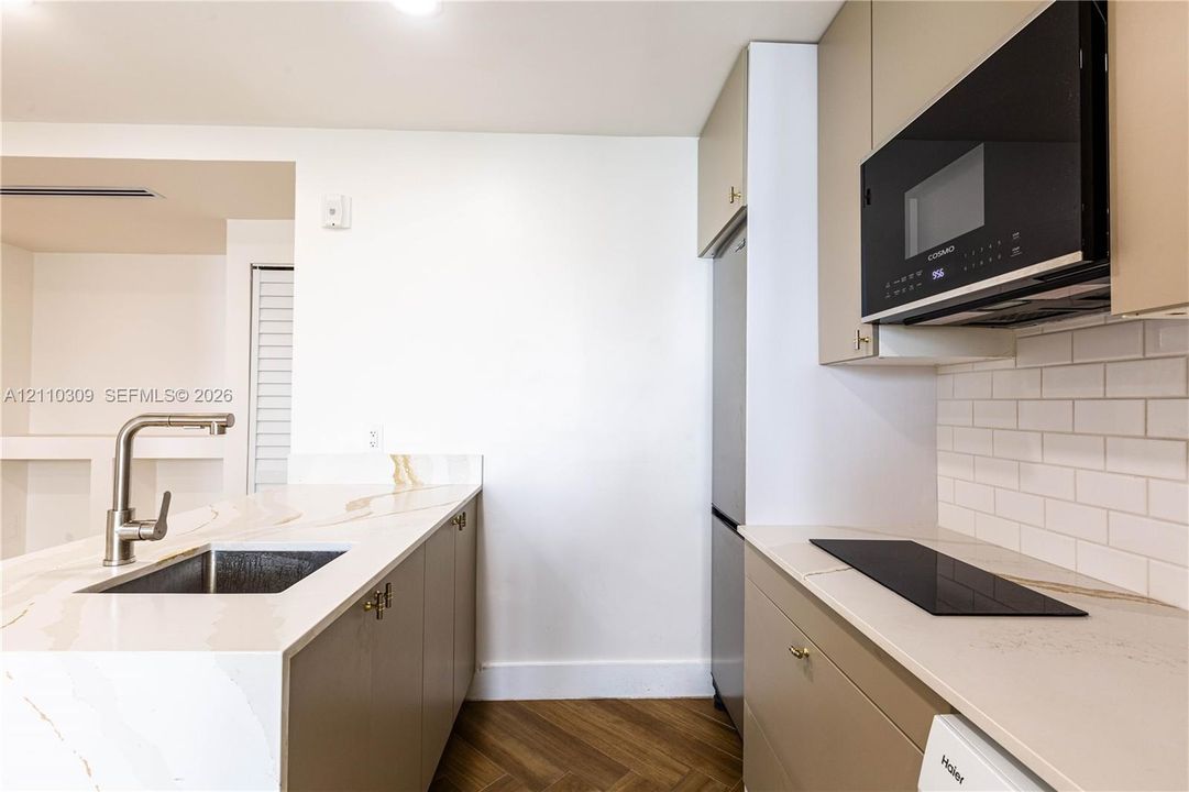 Kitchen featuring flat-panel cabinetry, light-toned stone-finish countertops, herringbone-patterned wood-finish flooring, a white subway-tile backsplash, and integrated stainless steel and black appliances