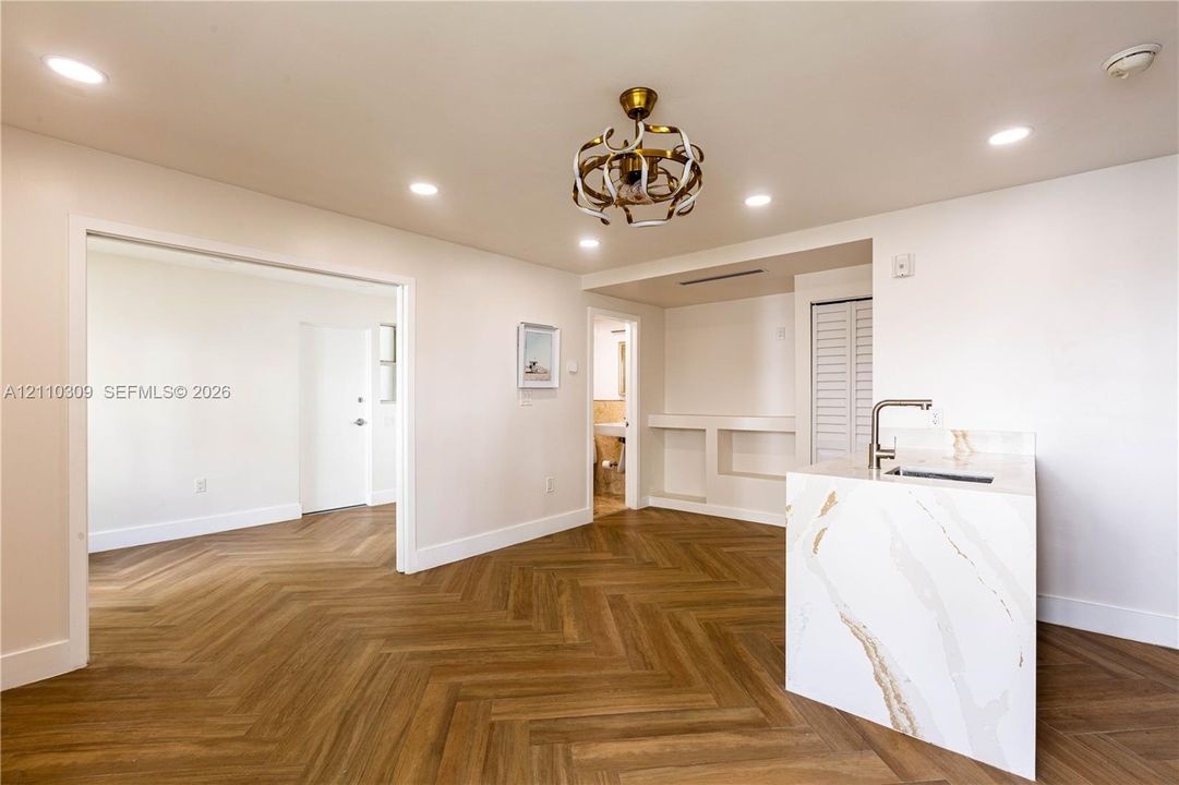 Interior space featuring wood-finish herringbone flooring, recessed lighting, a stone-surfaced kitchen island with an integrated sink, decorative chandelier, and built-in shelving