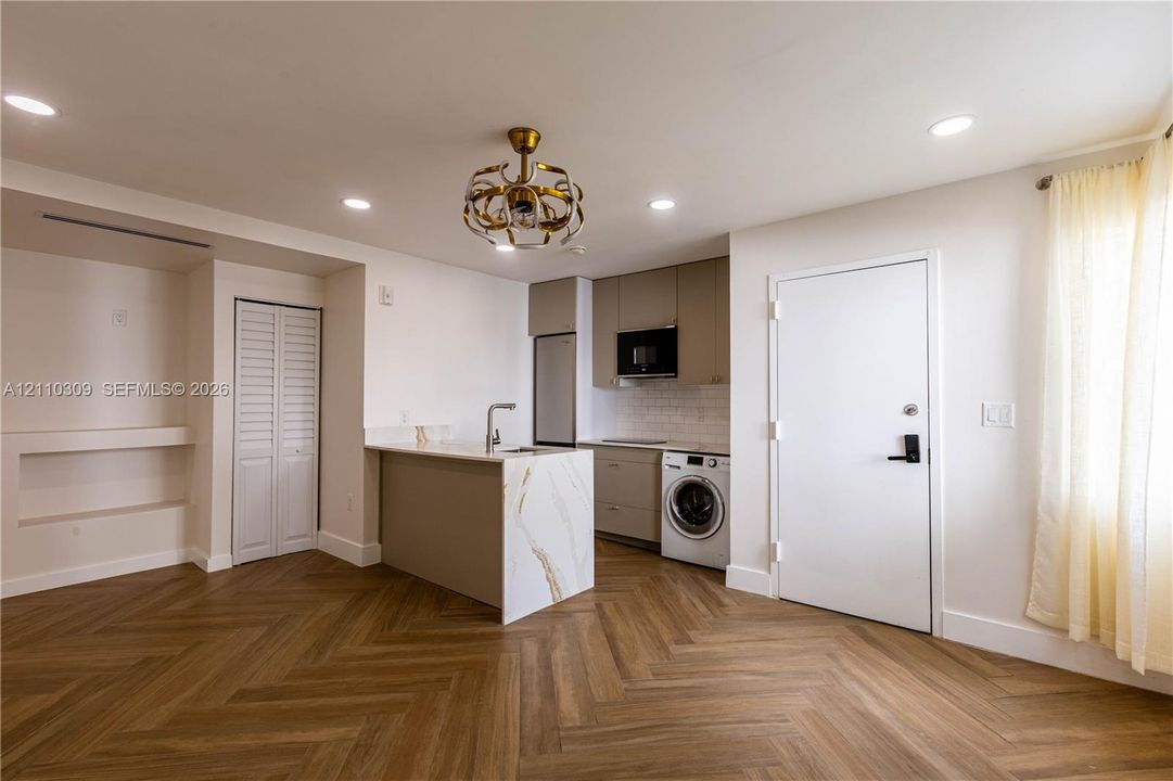 Herringbone wood-finish flooring, kitchen island with stone-finish waterfall countertop, built-in cabinetry, recessed lighting, and ornate metallic chandelier