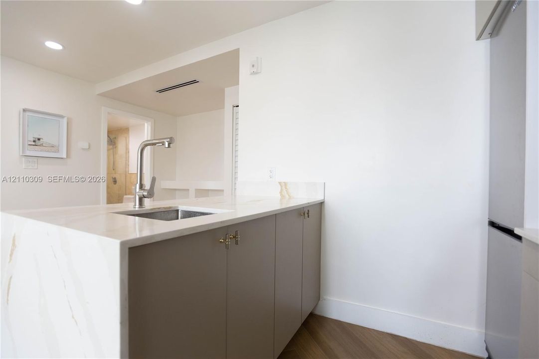 Kitchen island featuring a stone countertop with waterfall edge, undermount sink, high-arc faucet, and flat-panel cabinetry with metallic hardware