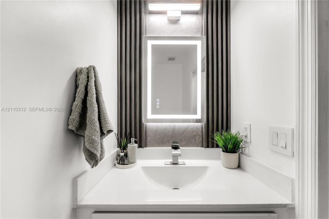 Integrated vanity featuring a solid surface countertop, undermount sink, LED-lit vanity mirror, and decorative fluted wall paneling