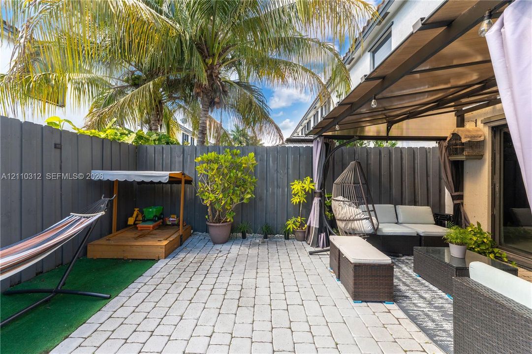 Private patio featuring stone paver flooring, overhead metal-framed structure, and full-height perimeter fencing