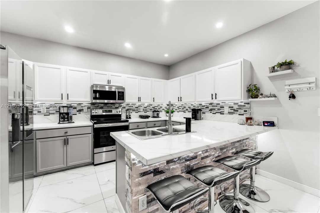 Kitchen featuring white upper cabinetry, grey lower cabinetry, white stone-finish countertops, stainless steel appliances, and a tiled backsplash
