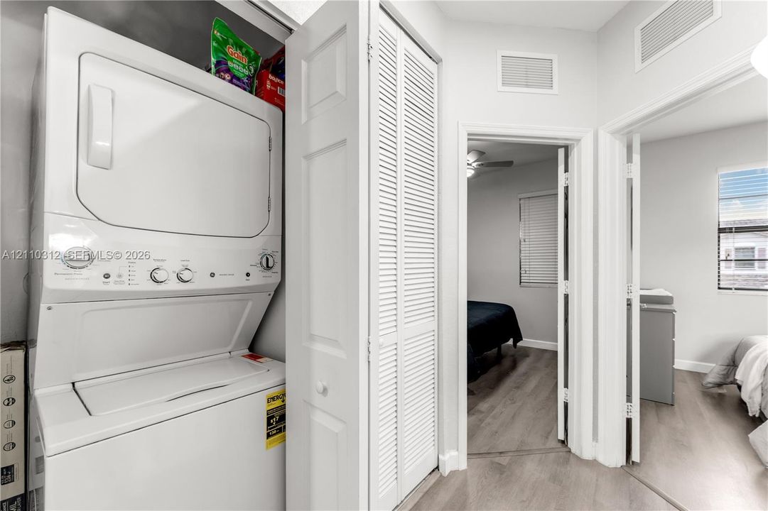 Laundry area featuring a stackable white washer and dryer unit concealed by louvered bi-fold doors